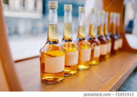 Bottles with a golden alcoholic beverage. Empty labels. Bottles of Rakia are on display in a row. Bottles with a golden alcoholic beverage. Empty labels. Bottles of Rakia are on display in a row. 72051413