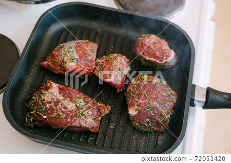Four raw steaks are fried on a grilled pan. 72051420