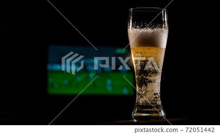 Close-up of fresh foaming light beer in a glass and football on TV on background. Sports bar concept 72051442