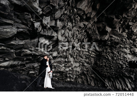 Destination Iceland wedding. Wedding couple under a rock of basalt stones. Bride and groom on the black beach of Vik. Destination Iceland wedding. Wedding couple under a rock of basalt stones. Bride and groom on the black beach of Vik. 72051448