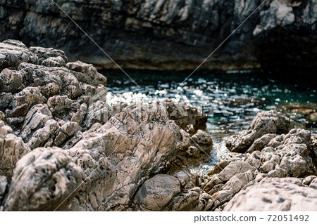 Rocky massive rocks near azure sea water and mountains. Rocky massive rocks near azure sea water and mountains. 72051492