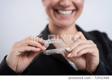 A woman is holding a transparent plastic mouth guard. Orthodontist's bite correction device 72052466