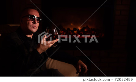Mature man drinking cognac by the fireplace. 72052499