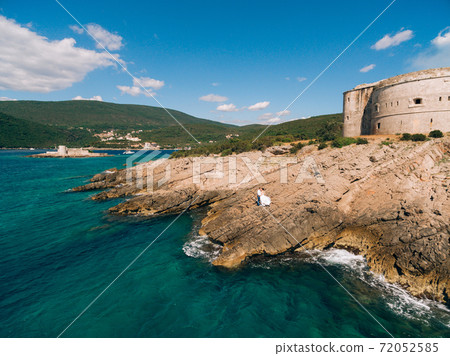 bride and groom are standing together and holding hands near the Arza fortress on the Mamula island bride and groom are standing together and holding hands near the Arza fortress on the Mamula island 72052585