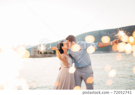 the bride and the groom kissing on the on the beach of the Mamula island and holding sparklers the bride and the groom kissing on the on the beach of the Mamula island and holding sparklers 72052741