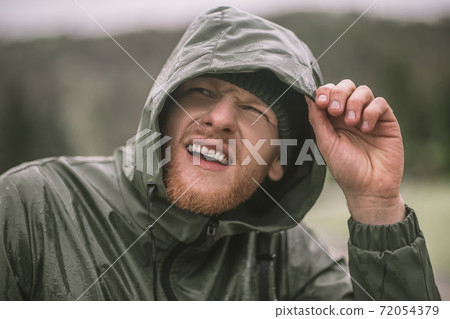 Young bearded man in a hood standing under the rain Young bearded man in a hood standing under the rain 72054379