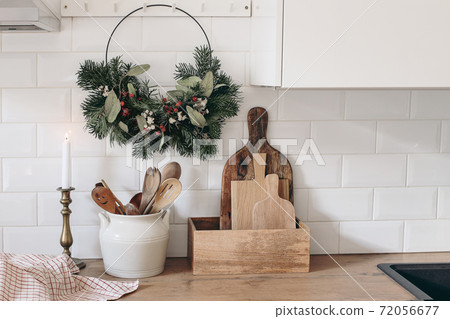 Closeup of kitchen interior. Christmas decoration. Advent floral hoop wreath hanging on peg rails. White brick wall, metro tiles, wooden countertops with kitchen utensils. Vintage scandinavian design. Closeup of kitchen interior. Christmas decoration. Advent floral hoop wreath hanging on peg rails. White brick wall, metro tiles, wooden countertops with kitchen utensils. Vintage scandinavian design. 72056677