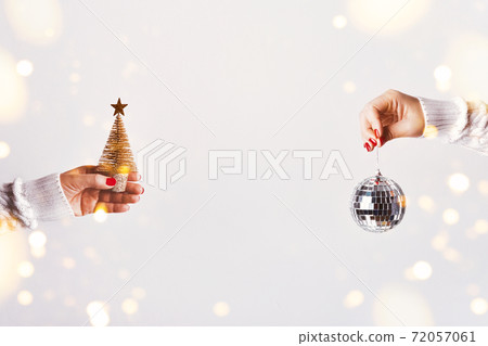 Female hands in white sweater holding golden Christmas tree and mirror disco ball on white background, copy space Female hands in white sweater holding golden Christmas tree and mirror disco ball on white background, copy space 72057061