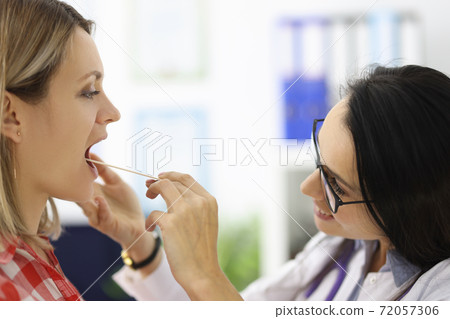 Doctor looking at patients throat with wooden spatula in clinic 72057306