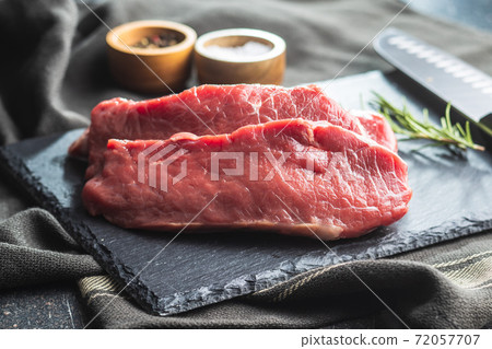 Slices raw striploin steak on black stone cutting board. Slices raw striploin steak on black stone cutting board. 72057707
