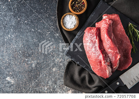Slices raw striploin steak on black stone cutting board. Slices raw striploin steak on black stone cutting board. 72057708