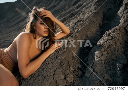 Woman posing, lying on dry cracked ground in quarry. Woman posing, lying on dry cracked ground in quarry. 72057997