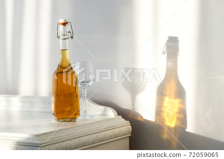 Elegant bottle with alcohol and empty glass over a vintage cabinet and a beautiful sun reflection on the wall - art concept 72059065