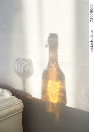 Elegant bottle with alcohol and empty glass over a vintage cabinet and a beautiful sun reflection on the wall - art concept Elegant bottle with alcohol and empty glass over a vintage cabinet and a beautiful sun reflection on the wall - art concept 72059066