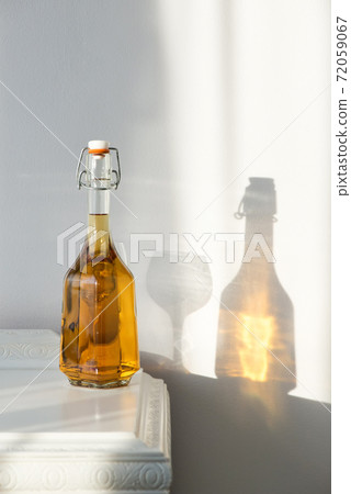 Elegant bottle with alcohol and empty glass over a vintage cabinet and a beautiful sun reflection on the wall - art concept Elegant bottle with alcohol and empty glass over a vintage cabinet and a beautiful sun reflection on the wall - art concept 72059067