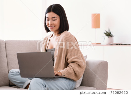 Asian woman sitting on couch and working on computer 72062620