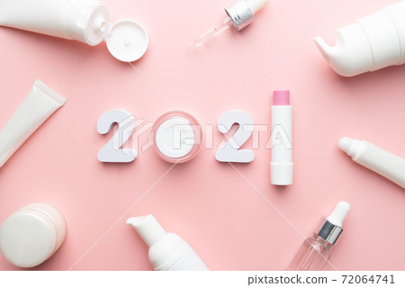 Best skincare products and cosmetic trends of 2021 concept. 2021 white number with lip balm, cream bottle, serum and lotion on pink background. Best skincare products and cosmetic trends of 2021 concept. 2021 white number with lip balm, cream bottle, serum and lotion on pink background. 72064741