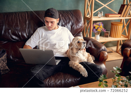 Young man working on laptop computer sitting at home with a dog pet and leaning during Coronavirus or Covid-19 quarantine Young man working on laptop computer sitting at home with a dog pet and leaning during Coronavirus or Covid-19 quarantine 72066252