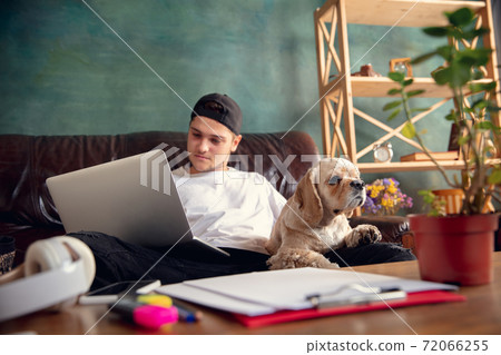 Young handsome man sitting and working at home with his cute dog. Cozy office workplace, remote work, online learning concept. 72066255