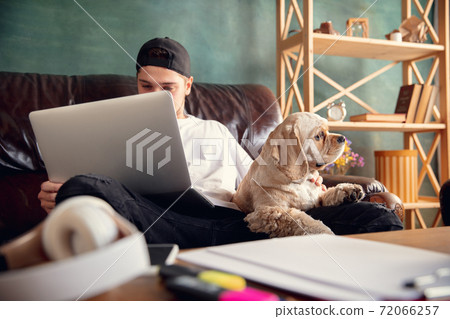 Young man working on laptop computer sitting at home with a dog pet and leaning during Coronavirus or Covid-19 quarantine Young man working on laptop computer sitting at home with a dog pet and leaning during Coronavirus or Covid-19 quarantine 72066257