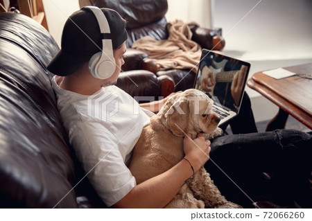Young man sitting at home with his dog pet and listening to music during Coronavirus or Covid-19 quarantine. Lifestyle concept. Young man sitting at home with his dog pet and listening to music during Coronavirus or Covid-19 quarantine. Lifestyle concept. 72066260