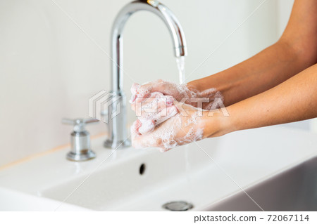 Woman washing her hands with soap in bathroom from side Woman washing her hands with soap in bathroom from side 72067114