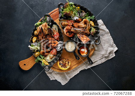 Mixed Roasted Seafood Platter Set. Contain Grilled Big Shrimps, Calamari Squids and Barracuda Fish Garlic Pepper with Spicy Chili Sauce and Potatoes, on wooden board and Black Background. 72067288