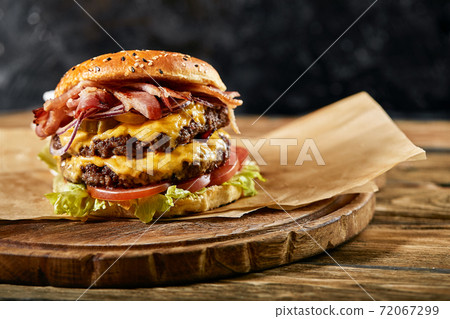 A large mouth-watering burger with grilled beef patty and fresh vegetables. Tasty american cheeseburger on a wooden board. Classic homemade burger in craft paper. A large mouth-watering burger with grilled beef patty and fresh vegetables. Tasty american cheeseburger on a wooden board. Classic homemade burger in craft paper. 72067299