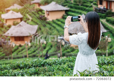 Happy tourist woman in white dress taking photo by mobile smartphone in beautiful Tea garden.Traveler visiting in Ban Rak Thai village, Mae Hong Son, Thailand. travel, vacation and holiday concept 72068072