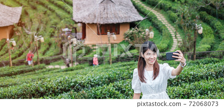 Happy tourist woman in white dress taking photo by mobile smartphone in beautiful Tea garden.Traveler visiting in Ban Rak Thai village, Mae Hong Son, Thailand. travel, vacation and holiday concept 72068073