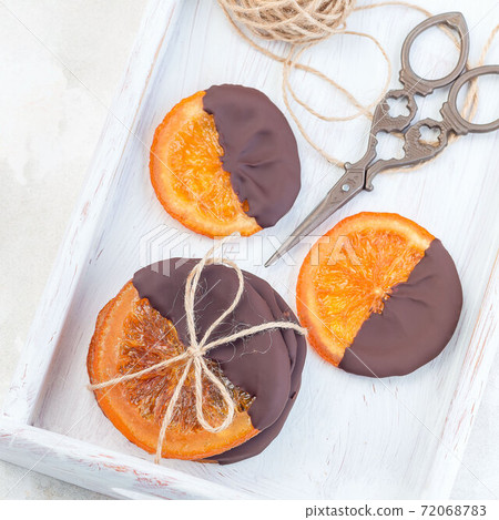 Candied sliced oranges covered with chocolate on a white tray, top view, square format Candied sliced oranges covered with chocolate on a white tray, top view, square format 72068783