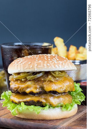 Double cheese burger with two beef patty, cheddar cheese, lettuce, caramelized onion and jalapeno slices, served with french fries and soda, on wooden board, vertical, copy space 72068796