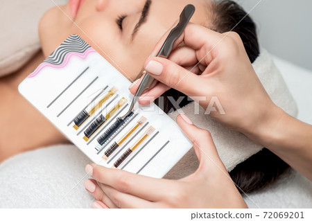 Beautician takes eyelashes by tweezers. Beautician takes eyelashes by tweezers. 72069201