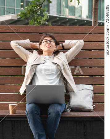 Freelance business woman sits in park with laptop and take away cardboard cup of coffee. Casual clothes, urban lifestyle of millennials. Working remotely. Freelance business woman sits in park with laptop and take away cardboard cup of coffee. Casual clothes, urban lifestyle of millennials. Working remotely. 72069888