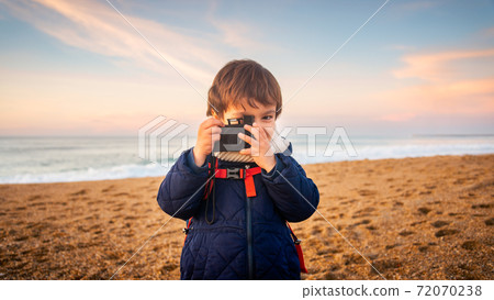 Little boy playing with camera on beach at sunset Little boy playing with camera on beach at sunset 72070238