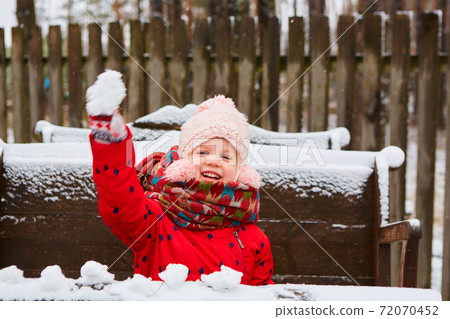 Winter girl throwing snowball at camera smiling happy having fun outdoors on snowing winter day playing in snow. Cute playful girl outdoor enjoying first snow 72070452