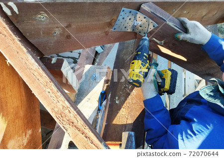 In a rafter of a roof the worker twists screws in a plate for screws using a screwdriver 72070644