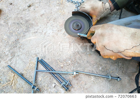 the worker uses an angle grinder to sharpen the bolts, a close-up plan the worker uses an angle grinder to sharpen the bolts, a close-up plan 72070663