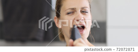 Woman holds comb in her hands and sings in front of mirror. 72072871
