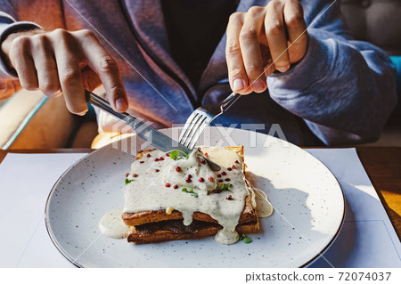 Close up of male hands holding a knife and fork and cutting sandwich Close up of male hands holding a knife and fork and cutting sandwich 72074037