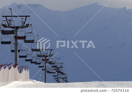 Snowy ski slope and chair lift on high mountains at winter evening 72074118