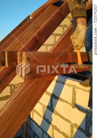 The worker claps the studs with a hammer on the rafters, building a roof 72074207