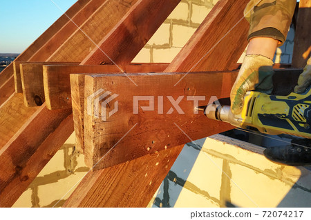 The worker uses a drill in the construction of the roof 72074217