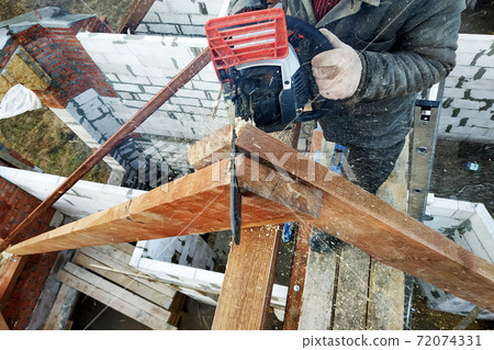 The builder saws on the roof of the chainsaw. Roof rafters. 72074331
