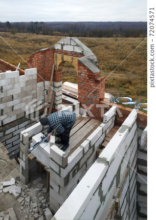 The master, using a trowel, glues gasblocks with a glutinous solution at the construction site The master, using a trowel, glues gasblocks with a glutinous solution at the construction site 72074571
