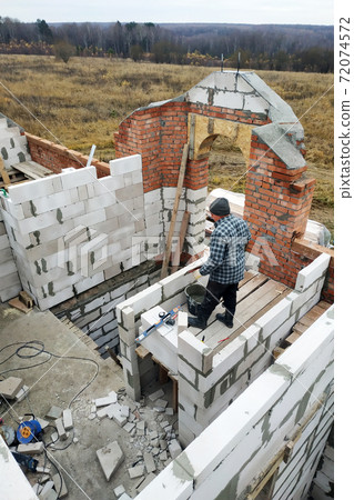 The master, using a trowel, glues gasblocks with a glutinous solution at the construction site 72074572