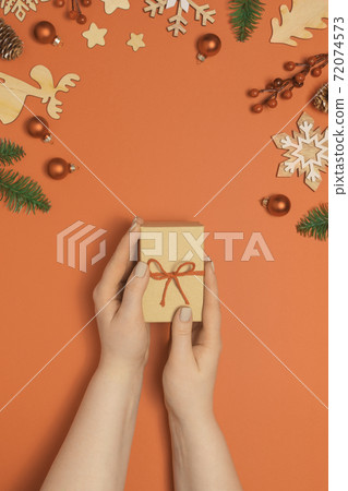 Woman holding present box on orange table 72074573