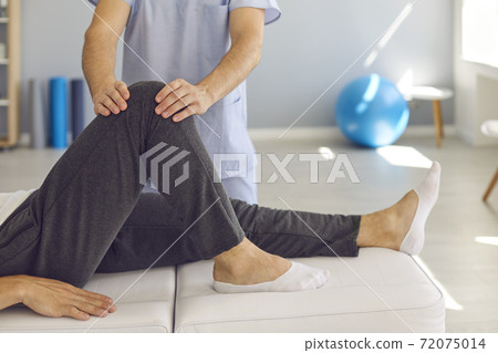 Hands of doctor masseur fixing patients knee in stable position during visit Hands of doctor masseur fixing patients knee in stable position during visit 72075014