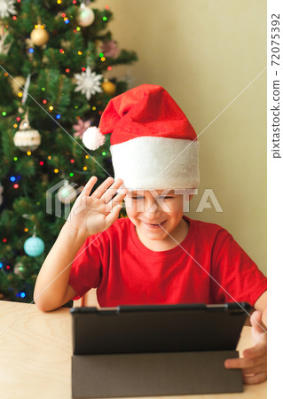 Cute little boy in red Christmas hat has video call using tablet Cute little boy in red Christmas hat has video call using tablet 72075392