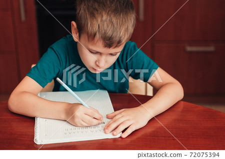 7 years old child writing letters in notebook sitting by table 7 years old child writing letters in notebook sitting by table 72075394